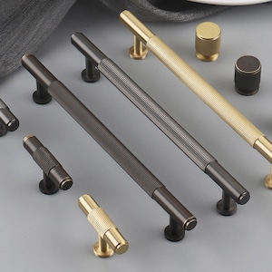 May include: A set of eight cabinet hardware pulls in two finishes: brushed brass and black. The pulls are all rectangular with a grooved design. There are two sizes of pulls, one long and one short.