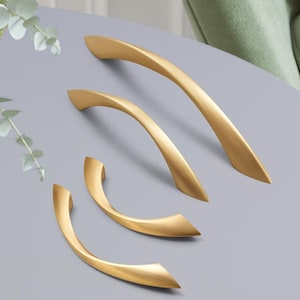 以下が含まれることがあります： 4つの異なるサイズと形の金色のキャビネットプル。プルは、最も大きいものから最も小さいものまで、一列に並んでいます。