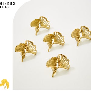 May include: Set of five gold-toned metal ginkgo leaf napkin rings. The rings are intricately designed with a delicate, openwork pattern.