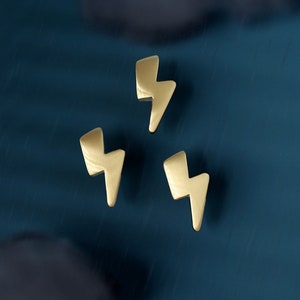 Può includere: Tre tiretti per cassetti a forma di fulmine dorati. I tiretti sono su uno sfondo blu scuro.