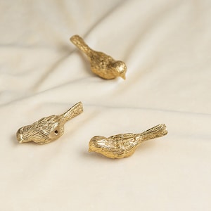 May include: Three gold bird-shaped decorative hooks. The hooks are made of metal and have a detailed design.