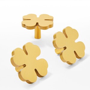 May include: Three gold-coloured metal cabinet knobs shaped like four-leaf clovers.