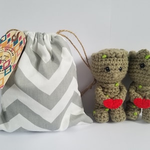 May include: Two small crocheted green Groot figures holding red hearts, in a gray and white chevron drawstring bag with a tag that says "All Things Creation".