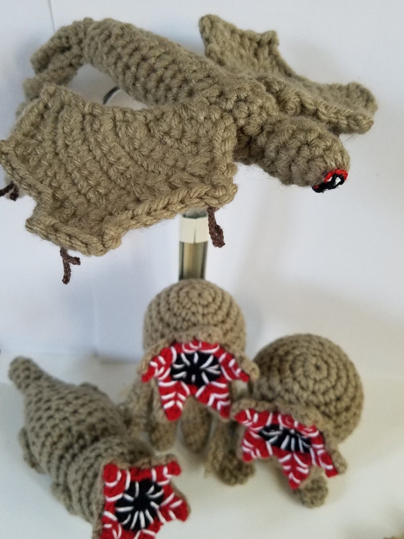 May include: Four crocheted plush toys in the shape of the creature from the movie "Stranger Things". The creature is brown with red and white eyes. One of the creatures is flying.