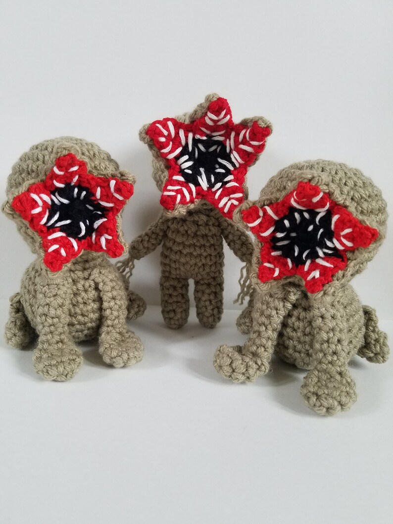 May include: Three crocheted plush toys shaped like the Demogorgon from the show Stranger Things. Each toy has a red and white mouth with black teeth and a beige body.