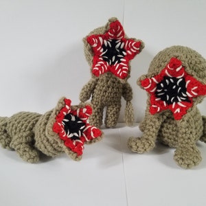 May include: Three crocheted plush toys shaped like the monster from the show Stranger Things. The toys are green and have a red and white mouth with black teeth.