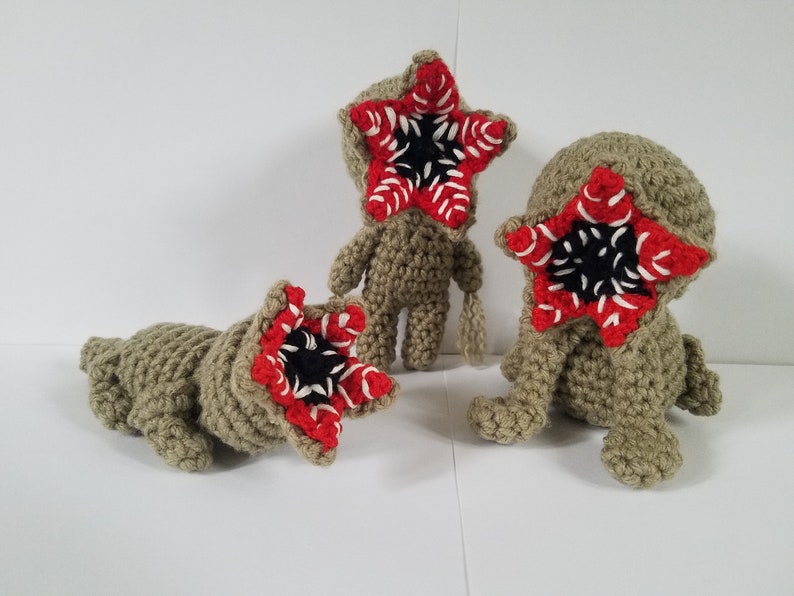 May include: Three crocheted plush toys shaped like the monster from the show Stranger Things. The toys are green and have a red and white mouth with black teeth.