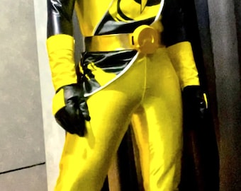 Puede incluir: Un traje de Power Ranger amarillo y negro con un casco blanco y un cinturón dorado. El traje tiene una franja blanca en el lateral y un diseño negro y amarillo en el pecho.