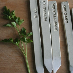 Könnte beinhalten: Vier weiße Keramik-Pflanzenmarkierer mit den Worten "Dill", "Petersilie", "Schnittlauch" und "Oregano" darauf.