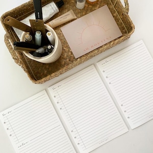 May include: Three white lined pages with holes on the left side. The pages are labeled "to do" and "notes". The pages are on a white surface. A wicker tray with various items is in the background.