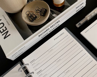 May include: A black and white password log book with a white background and black lines. The book has a clear plastic ring binder and the words "PASSWORDS" are printed in black at the top of the page. The book is open to a page with the heading "WEBSITE" and columns for "USERNAME", "SECURITY QUESTION", "NOTES", and "PASSWORD".