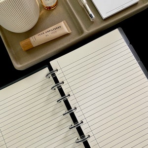 May include: An open notebook with lined pages and a binder, next to a tray with a pen, lip balm, and a bottle of rose hibiscus oil. The notebook is open to a blank page, ready for notes.