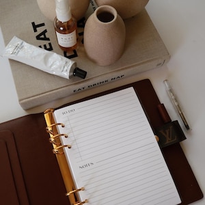 May include: A brown leather bound planner with gold rings and a white page insert. The page has lines for writing notes and a section labeled "To Do" and "Notes".