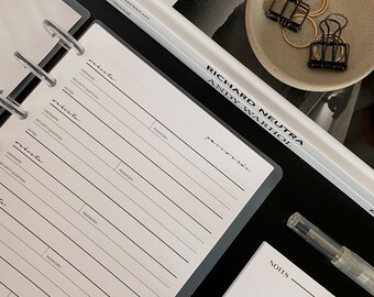 May include: A black and gray six-ring binder with a white page open to a password log. The page has fields for username, security question, notes, and password. The binder is on a black surface.