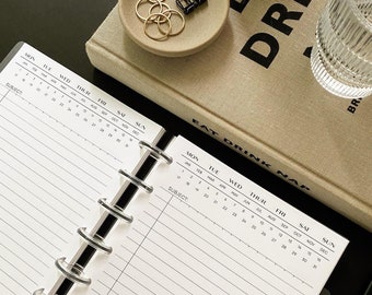 Op de afbeelding: Een zwart-witte maandplanner met een zwarte spiraalbinding. De planner heeft een witte achtergrond met zwarte tekst en lijnen. De planner is open voor de maand januari en de onderwerpregel is zichtbaar.