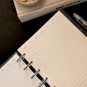 May include: A black and white planner with a clear plastic cover and a black metal binding. The planner has a monthly calendar layout with the months of January through December. The planner also has a section for notes and a subject line.
