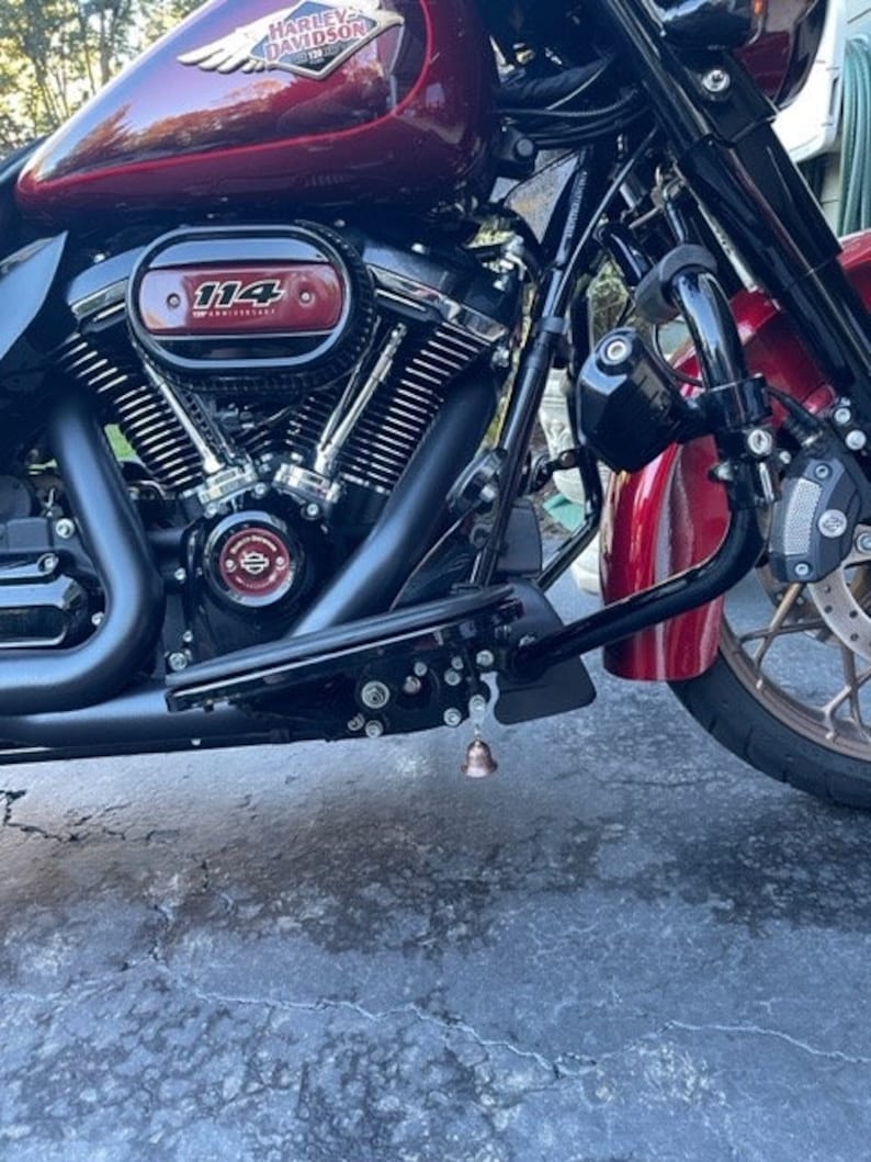 May include: Close-up of a red Harley Davidson motorcycle with a black engine and a chrome air filter. The motorcycle has a black bell hanging from the bottom of the frame.