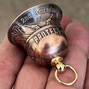 May include: A copper bell with a gold ring. The bell is engraved with the words "The 2nd Amendment Est 1791" and "Protect".