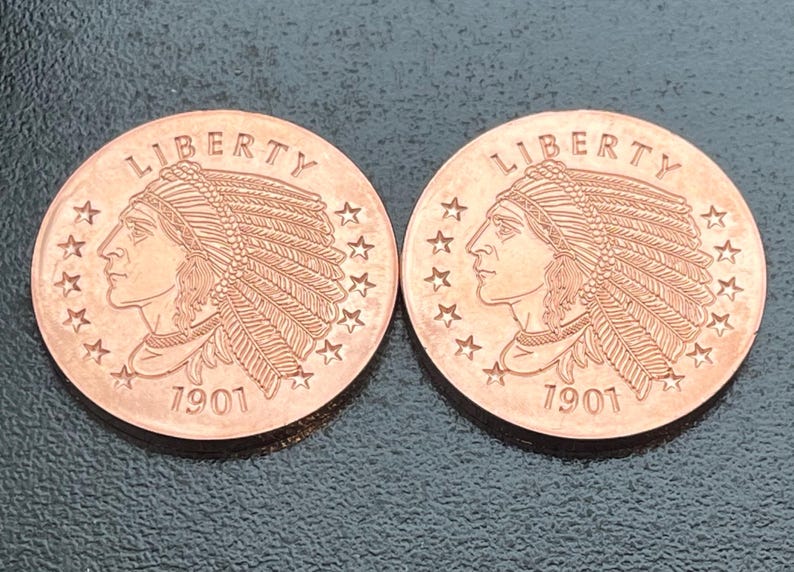 May include: Two copper-colored round coins featuring the profile of a person wearing a feathered headdress. The word LIBERTY is arched at the top, and the year 1901 is printed at the bottom. Thirteen stars are arranged along the coin edge.