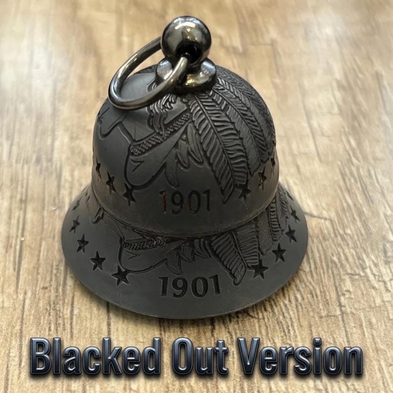 May include: A matte black metal bell featuring an engraved feather design, a ring of small stars around the base, and the number 1901 etched into the surface. A circular metal loop is attached to the top of the bell for hanging purposes.