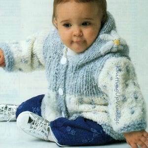 May include: A baby wearing a light blue and white knitted hooded sweater with a daisy detail on the hood. The sweater has three white buttons and is paired with dark blue pants and white shoes. The text "KnittingUpVintage" is on the sleeve.