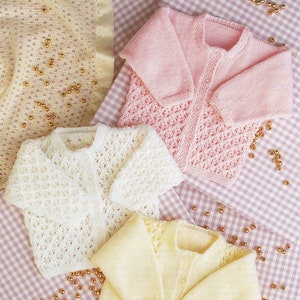 May include: Three knitted baby cardigans in pink, white and yellow with a lacy pattern. The cardigans are laid out on a pink and white gingham fabric.