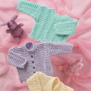 May include: Three knitted baby sweaters in different colors: light green, lavender, and cream. The sweaters have a wavy stitch pattern and button closures.