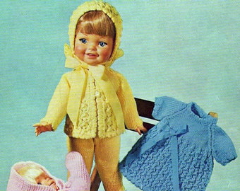 May include: A doll wearing a yellow knitted cardigan and pants, a pink knitted hooded coat, and a blue knitted dress. The doll is sitting on a wooden chair.