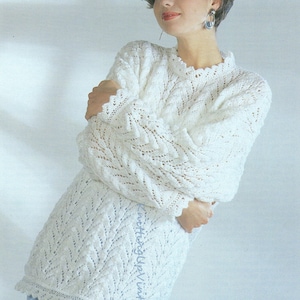 May include: A white crocheted sweater with a delicate lace pattern. The sweater has a round neckline and long sleeves. The model is wearing the sweater with a blue and white checked skirt.