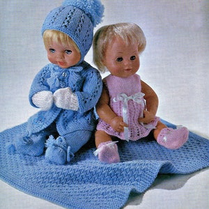 Può includere: Due bambole di lana, una con un completo di lana blu con un cappello bianco con pon pon e l'altra con un vestito di lana rosa. Entrambe le bambole sono sedute su una coperta di lana blu.