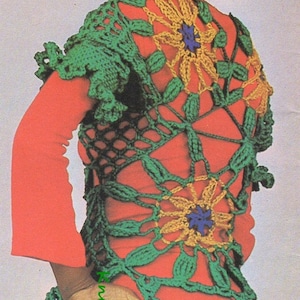 May include: A woman wearing a red jumpsuit with a green crocheted vest featuring a floral design. The vest has yellow and blue flowers.