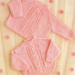 May include: Two pink knitted baby cardigans with button closures and a delicate lace pattern.