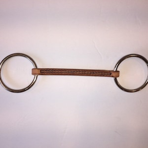 May include: A brown leather horse bit with two silver rings.