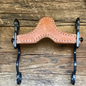 May include: A horse bit featuring a tan leather noseband with white stitching, connected to two black metal shanks. The shanks have curved designs and circular rings at the top and bottom, providing a functional piece of equestrian equipment.