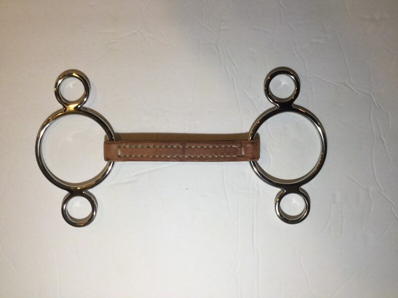 Puede incluir: Un bocado de caballo de plata con una correa de cuero. El bocado tiene tres anillos a cada lado.