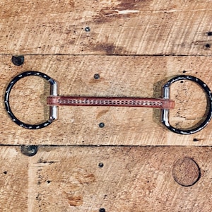Op de afbeelding: Een bruin lederen paardenbit met twee zwarte metalen ringen. Het bit is ontworpen voor gebruik met een paardenhoofdstel.