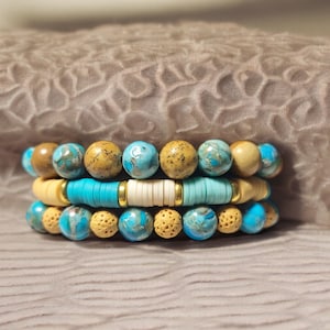 Peut inclure: Quatre bracelets empilés avec des perles bleues et brunes. Le bracelet du haut a des perles bleu clair et blanches, le deuxième bracelet a des perles bleu clair et brunes, le troisième bracelet a des perles bleu clair et brunes, et le bracelet du bas a des perles bleu clair et brunes.