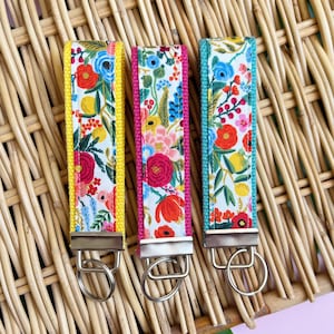 May include: Three keychains with floral fabric and metal rings. The keychains are yellow, pink, and teal.