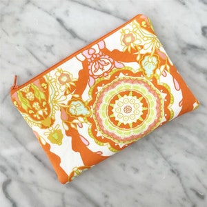 May include: Orange and white zippered pouch with a paisley pattern. The pouch has a white background with orange, pink, green, and blue paisley designs.