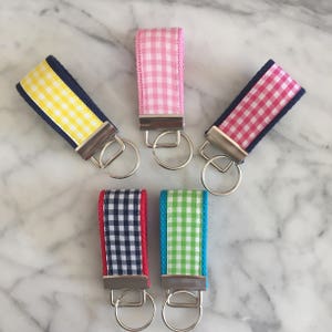 May include: Five keychains with different colored gingham patterns. Each keychain has a silver key ring. The keychains are on a white marble surface.