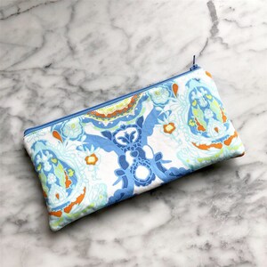 May include: A blue and white paisley patterned zippered pouch. The pouch is made of fabric and has a white background with blue, orange, and green paisley designs.