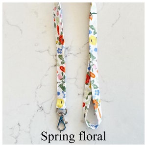 Peut inclure: Un cordon blanc avec un motif floral dans des tons de rouge, orange, jaune, bleu et vert. Le cordon a un clip argent&eacute; &agrave; une extr&eacute;mit&eacute;. Le texte "Spring floral" est imprim&eacute; sous le cordon.