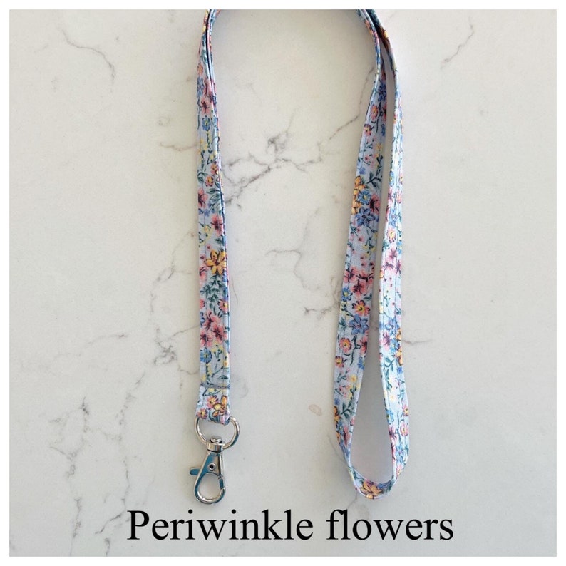 Peut inclure: Un cordon bleu clair avec un motif floral compos&eacute; de fleurs bleu pervenche, jaunes et roses. Le cordon a un clip argent&eacute; &agrave; une extr&eacute;mit&eacute;.