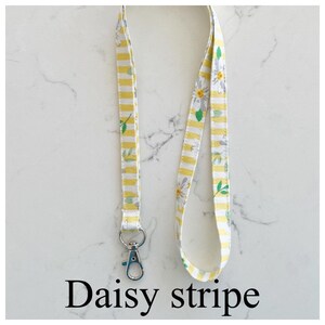 Peut inclure: Un cordon blanc et jaune ray&eacute; avec un imprim&eacute; de marguerite et un clip argent&eacute;. Le cordon porte l'inscription "Daisy stripe".