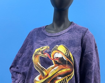 May include: Purple tie-dye t-shirt with a graphic print of a gold snake wrapped around a gold tongue. The tongue is dripping gold.