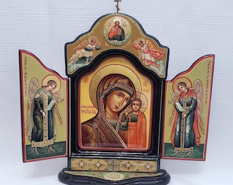 Pode incluir: Um ícone tríptico de madeira com fundo preto e detalhes dourados. O painel central apresenta uma pintura da Virgem Maria e o menino Jesus. Os painéis laterais apresentam pinturas de anjos com asas. O texto no ícone diz "Казанская Пресвятая Богородица" e "Слава Тебе Боже".