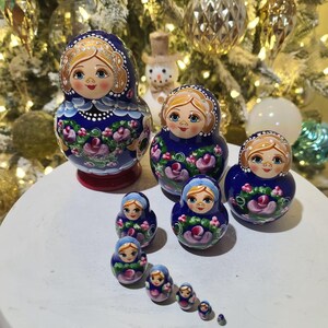 May include: A set of Russian nesting dolls, or Matryoshka dolls, in various sizes. The dolls feature a blue background with floral and gold accents. The largest doll is approximately 6 inches tall.