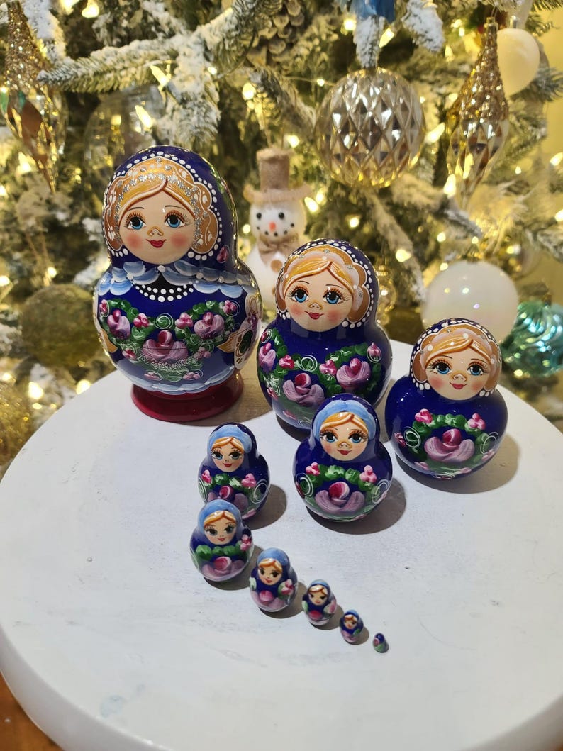 May include: A set of Russian nesting dolls, or Matryoshka dolls, in various sizes. The dolls feature a blue background with floral and gold accents. The largest doll is approximately 6 inches tall.