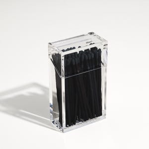 May include: A clear acrylic box filled with black matches. The box is rectangular and has a lid.