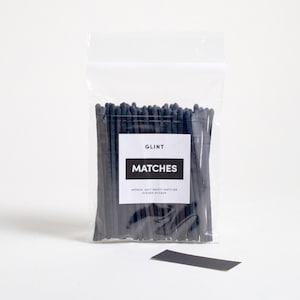 May include: A clear plastic bag filled with black matches. The bag has a white label that reads "GLINT MATCHES APPROX. 80CT SAFETY MATCHES STRIKE ON STICKER".